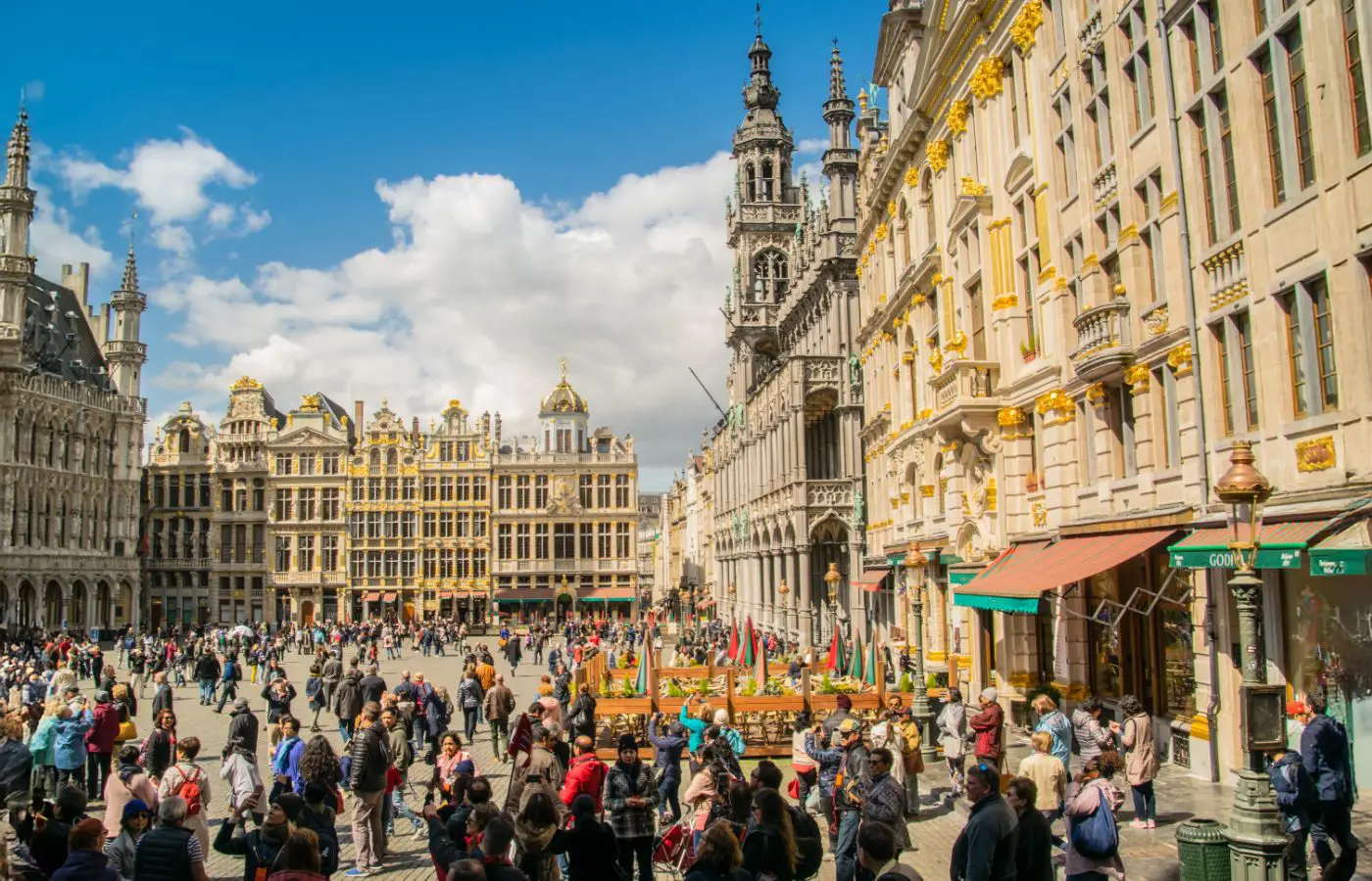 Vue animée de la Grand-Place de Bruxelles avec ses bâtiments historiques et une foule de visiteurs sous un ciel ensoleillé.