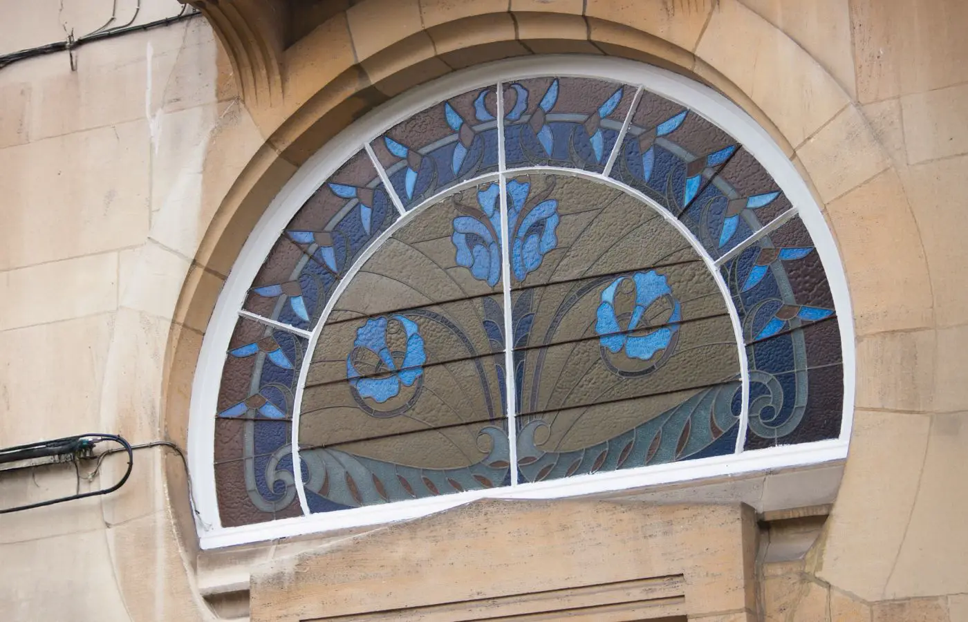 Vitrail de style Art Nouveau avec motifs floraux, encastré dans une arche en pierre beige, typique de l'architecture bruxelloise.