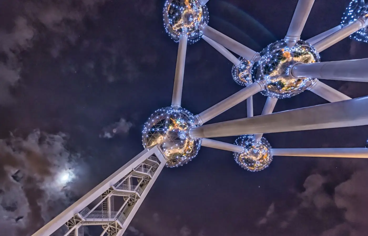 Vue nocturne spectaculaire de l'Atomium illuminé, avec ses sphères métalliques étincelantes et le ciel étoilé en arrière-plan, à Bruxelles.