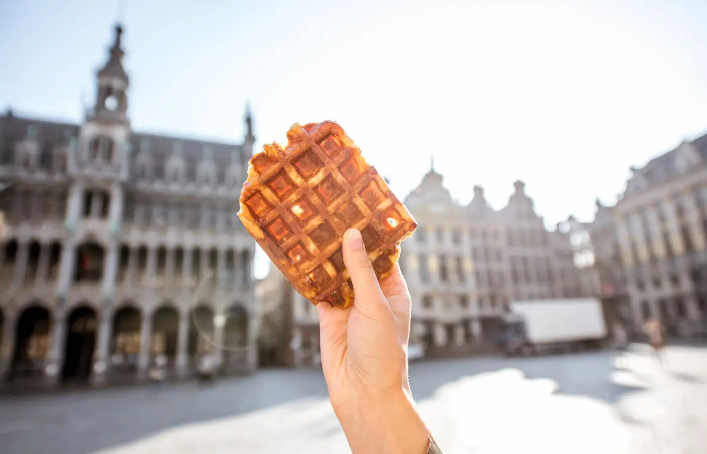 Main tenant une gaufre belge devant la Grand-Place de Bruxelles, symbole de la gastronomie et de l'art de vivre bruxellois.