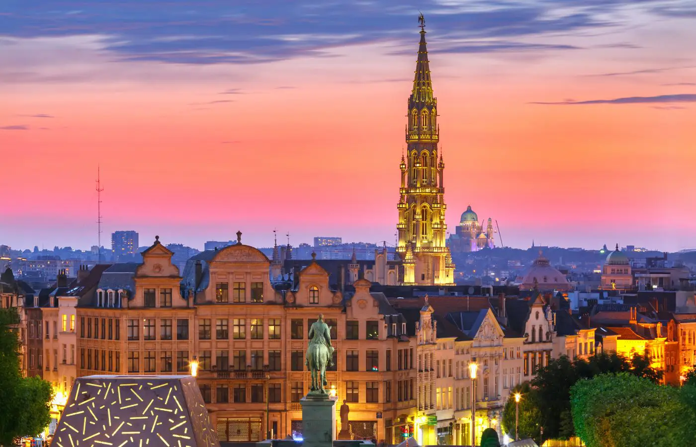 Vue panoramique de Bruxelles au coucher du soleil, mettant en valeur l'architecture emblématique et la tour de l'Hôtel de Ville sur la Grand-Place.