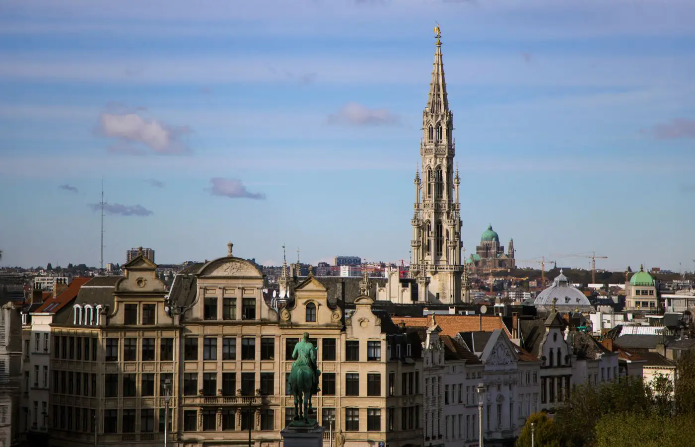 Vue panoramique de Bruxelles avec la tour de l'Hôtel de Ville dominant le paysage, entourée de bâtiments historiques sous un ciel bleu.